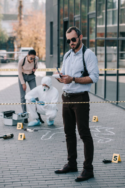 male detective standing at crime scene and making some notes