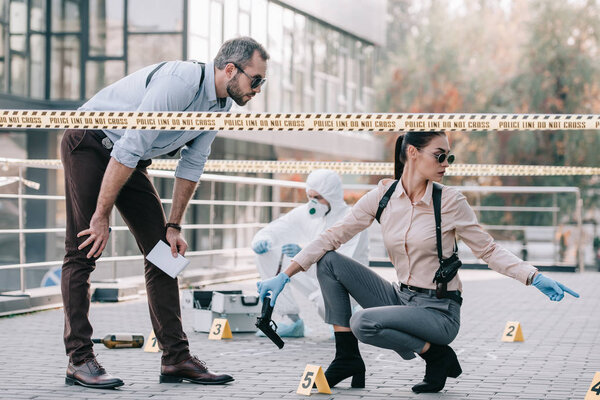 female and male detectives in sunglasses together inspect the crime scene