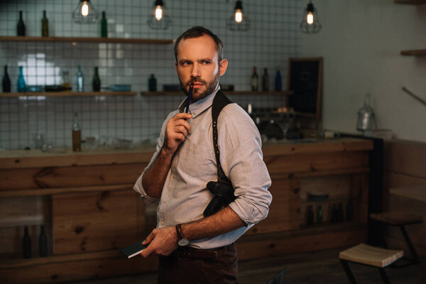 male detective sitting at crime scene holding pen near his mouth
