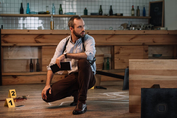 Serious male detective sitting at crime scene with notebook