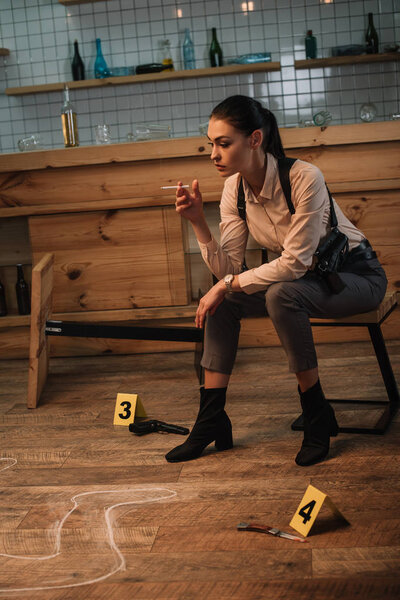 focused smoking female detective sitting at crime scene with evidence markers and dead body outline