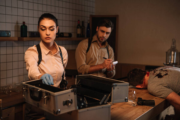 концентрированные детективы-женщины и мужчины используют набор для сбора улик и расследования трупа на месте преступления вместе
