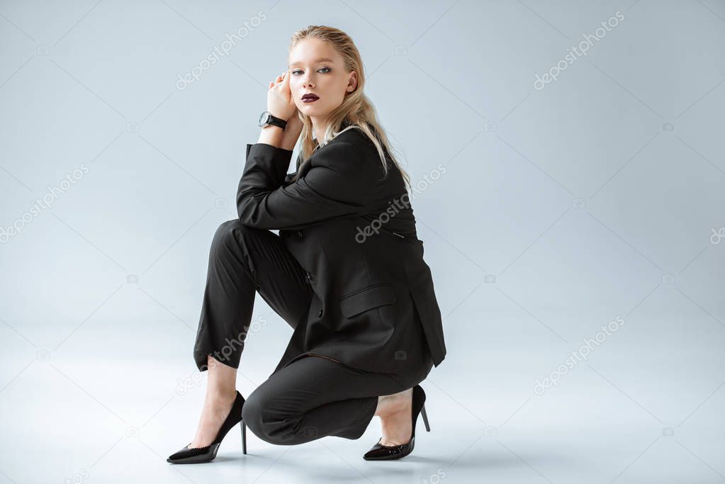 elegant young woman posing in trendy black suit on grey