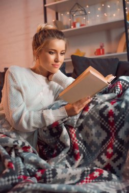 güzel gülümseyen kadın kitap okumak evde desenli battaniye içinde Noel arifesinde
