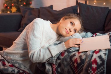 beautiful woman with book dreaming on sofa clipart