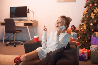 Sarışın genç kadın kanepede oturan ve smartphone üzerinde konuşurken Noel anda gülüyor 