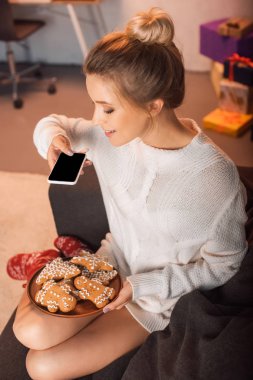Noel zamanda kanepe ve gingerbread çerezleri smartphone ile resmini alarak oturan genç sarışın kadının görüş açısı
