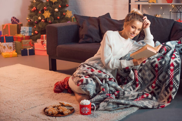 Очаровательная девушка улыбается и читает книгу дома в канун Рождества
