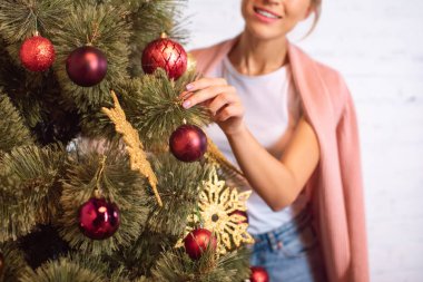 cropped view of young woman decorating christmas tree with baubles clipart