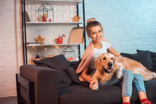 Bela Jovem Loira Sentada Sofá Abraçando Cão Golden Retriever Sorrindo — Fotografia de Stock