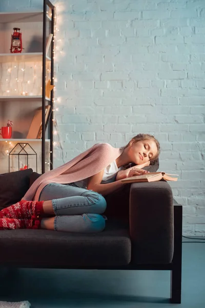 クリスマスの時に本でソファで寝ている金髪の若い女性 — ストック写真