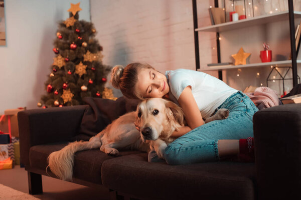 beautiful content young blonde woman on couch hugging golden retriever dog at christmas time