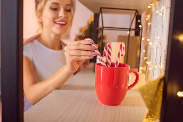 微笑的年轻金发碧眼的女人把糖果棒在红色杯在圣诞节时间 — 图库照片