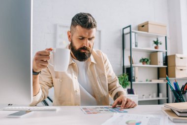 Erkek tasarımcı oturma ile beyaz fincan çay ve palette office bakarak