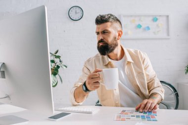 İçecek İçme ve modern ofiste bilgisayar monitörü bakarak yakışıklı Tasarımcısı 
