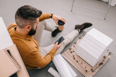 açı görünümünü smartphone kullanarak, kahve holding ve planları ofiste çalışan yetişkin erkek mimar sakallı 