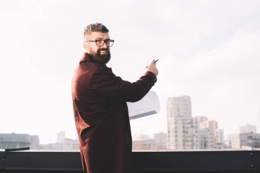 Yetişkin erkek mimar blueprint çatıda tutan gözlük gülümseyen