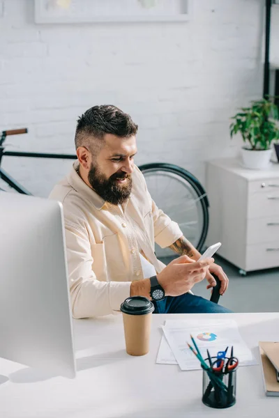 Χαμογελώντας Γενειοφόρος Επιχειρηματία Που Κάθεται Στο Γραφείο Και Κοιτάζοντας Smartphone — Φωτογραφία Αρχείου