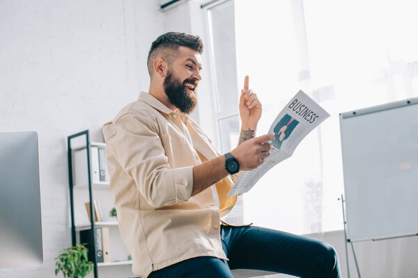 Cheerful businessman reading newspaper in modern office