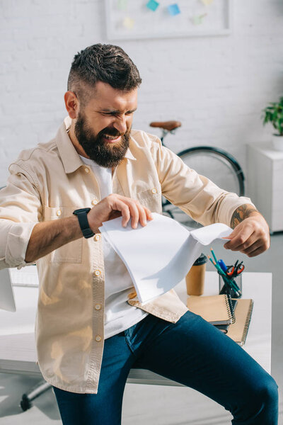 Aggressive boss tearing papers and sitting in modern office 