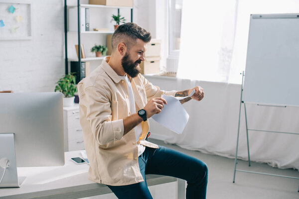 Angry casual businessman tearing papers in modern office 