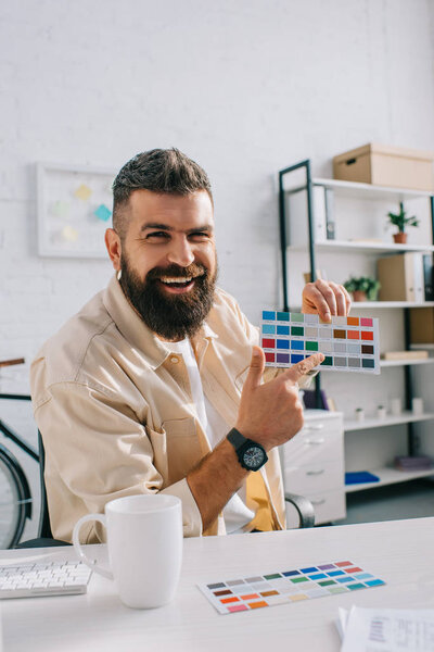 Handsome designer pointing at color palette in modern office