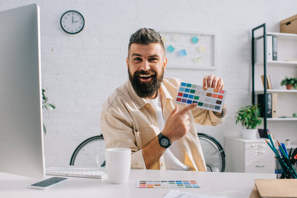 Bearded designer gesturing at color palette in modern office