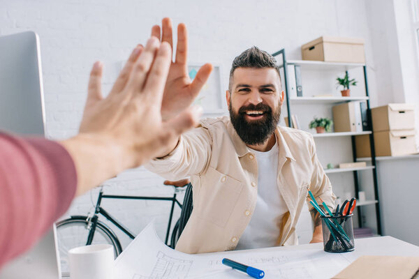 Smiling architect giving high five to coworker at modern office