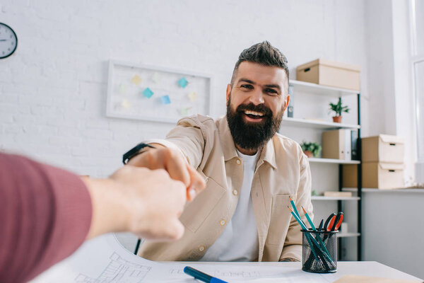 Cheerful architect smiling and giving fist bump to coworker in modern office