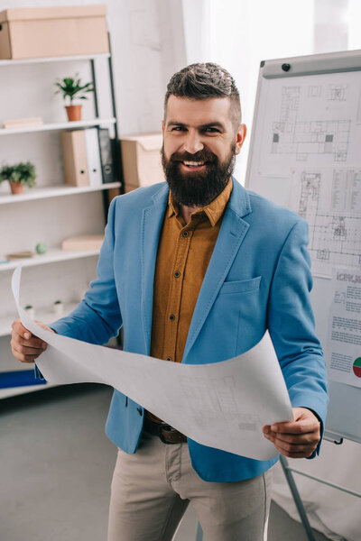 Handsome architect smiling and holding blueprint in modern office