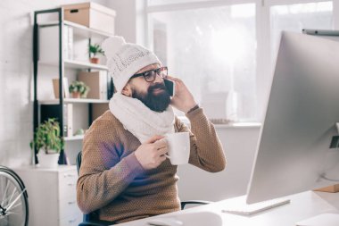 eşarp ve çay tutarak ve işyerinde Smartphone cep telefonu ile konuşurken örme şapka hasta iş adamı