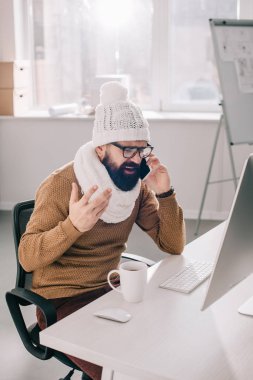 eşarp ve ofis masası oturma ve telefonda konuşurken örme şapka hasta iş adamı 