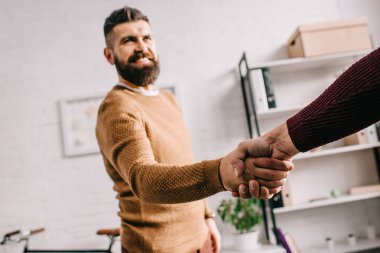 selective focus of smiling adult man shaking hands with partner in office clipart