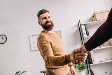 smiling adult businessman shaking hands with partner in office clipart