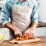 Junger Mann in Schürze schneidet frischen Pfeffer in Küche