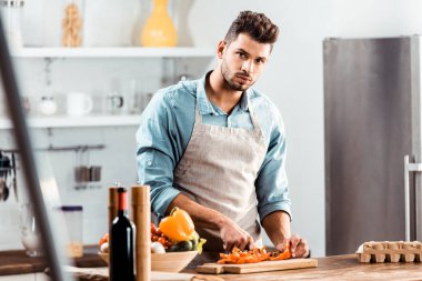 yakışıklı delikanlı sebze kesme ve mutfak kamerada bakarak önlük