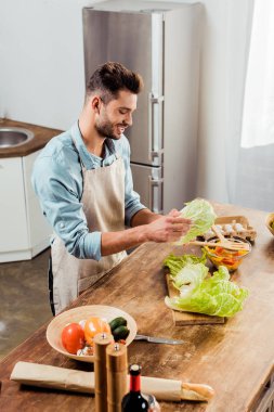 delikanlı mutfakta sebze salatası hazırlama önlük gülümseyen, yüksek açılı görünüş