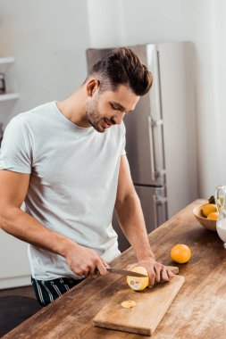 Genç adam Doğrama Kurulu mutfakta üzerinde limon kesme pijama gülümseyen