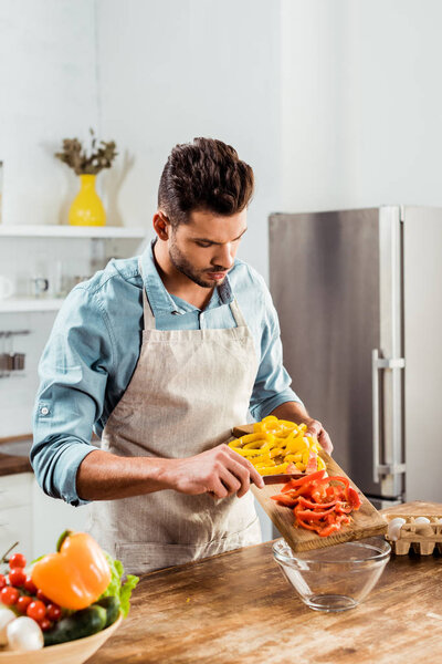 handsome young man in apron preparing vegetable salad in kitchen 