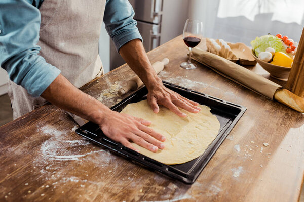 обрезанный снимок человека, готовящего тесто для пиццы на подносе
