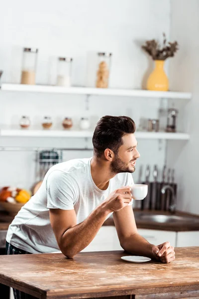 Sonriente Joven Sosteniendo Una Taza Café Mirando Hacia Cocina Por — Foto de stock gratis