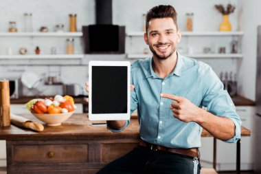 Dijital tablet boş ekran ile tutarak ve mutfak kameraya gülümseyen yakışıklı delikanlı 