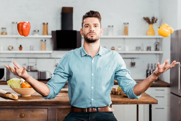 Joven Guapo Haciendo Malabares Con Pimientos Frescos Mirando Cámara Cocina — Foto de stock gratis