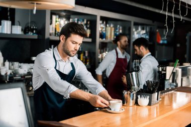 yakışıklı barista kahve fincanı ahşap kasada koyarak önlük