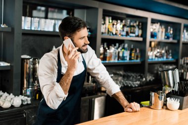 Smartphone üzerinde konuşmak ve önlük ayakta barmen çubuk 