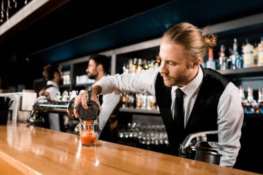 Barman pouring cocktail in glass on bar counter clipart