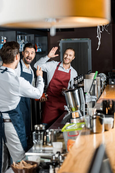 cheerful barmen in aprons high five at workplace