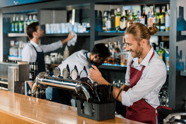 smiling barman pouring beer behind wooden counter at bar