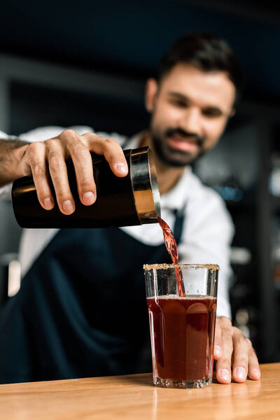 barman pouring cocktail from shaker in decorated glass at wooden counter