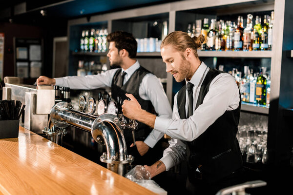Handsome barman standing and working with coworker in bar